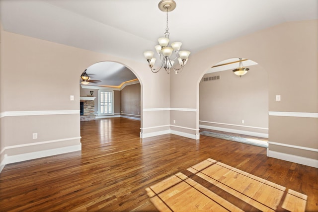 unfurnished room featuring a fireplace, ceiling fan with notable chandelier, and dark hardwood / wood-style floors