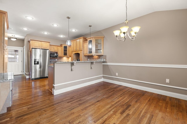 kitchen with stainless steel refrigerator with ice dispenser, a kitchen bar, decorative backsplash, hanging light fixtures, and vaulted ceiling