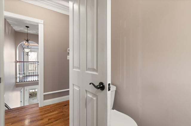 interior space with wood-type flooring, toilet, ornamental molding, and a notable chandelier