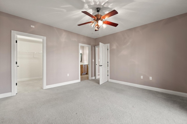 unfurnished bedroom with ensuite bathroom, a walk in closet, a closet, light colored carpet, and ceiling fan