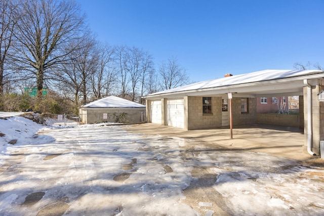 snow covered house with a carport, an outbuilding, and a garage