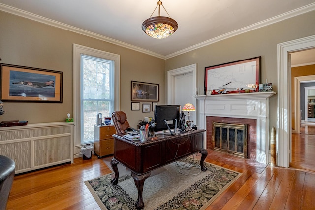 office area with wood-type flooring, radiator heating unit, crown molding, and a fireplace