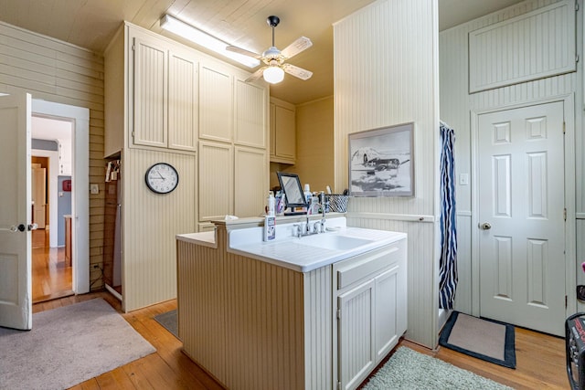 kitchen featuring sink, kitchen peninsula, light hardwood / wood-style floors, and wooden walls