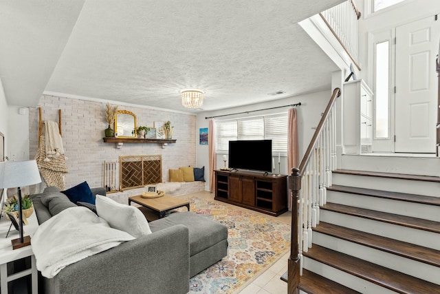 tiled living room with a brick fireplace, a notable chandelier, a textured ceiling, and brick wall