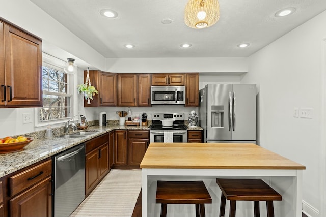 kitchen with stainless steel appliances, light stone countertops, sink, and a kitchen breakfast bar