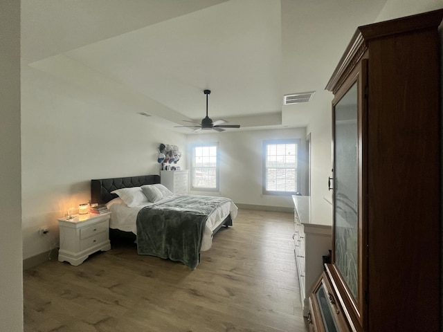 bedroom featuring a raised ceiling, ceiling fan, and light wood-type flooring