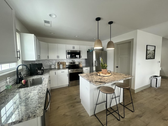 kitchen with appliances with stainless steel finishes, sink, white cabinets, a center island, and light stone counters