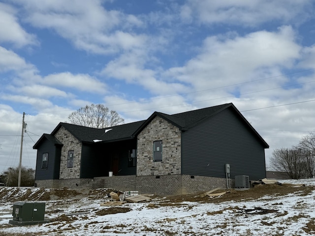 view of snow covered exterior with stone siding and cooling unit