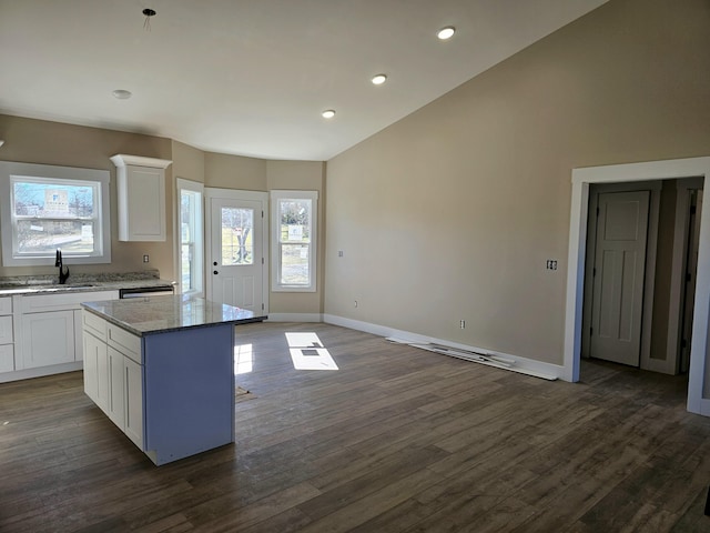 kitchen with dark wood-style flooring, a kitchen island, a sink, white cabinetry, and baseboards