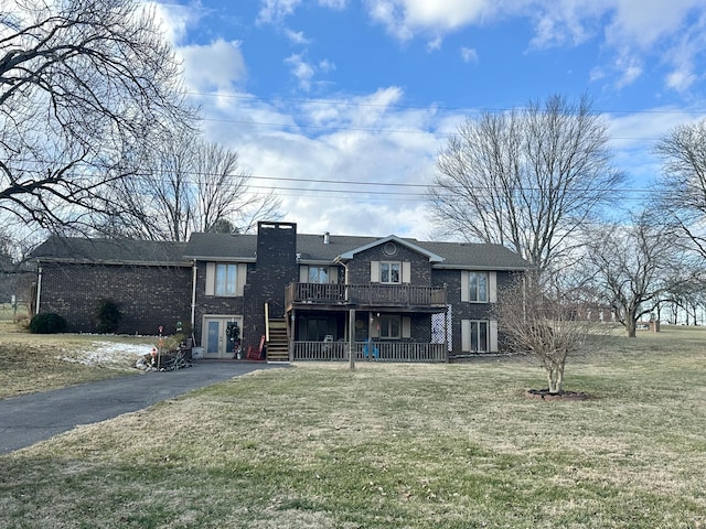 view of front facade with aphalt driveway, brick siding, a chimney, a deck, and a front lawn