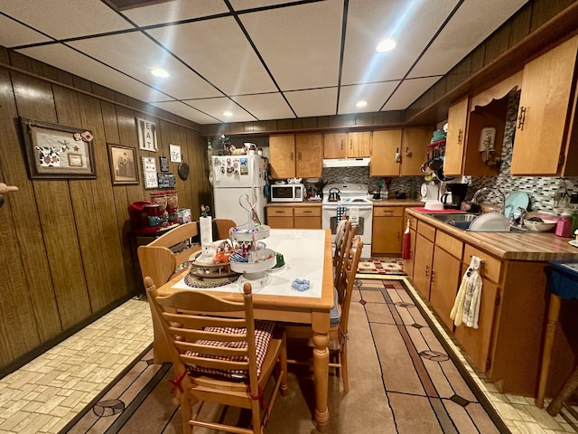 kitchen with sink, white appliances, wood walls, and backsplash