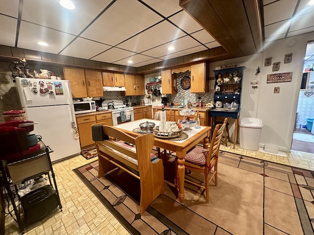 kitchen featuring white appliances, a drop ceiling, and backsplash