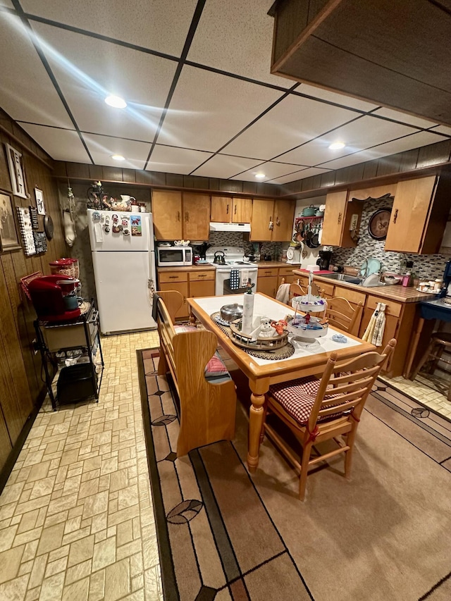 kitchen featuring backsplash, white appliances, a paneled ceiling, and wood walls