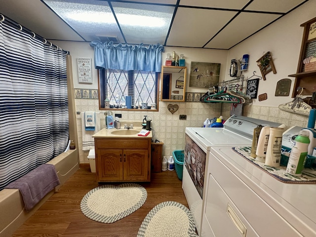 bathroom with wood-type flooring, tile walls, vanity, shower / bath combination with curtain, and washer and clothes dryer