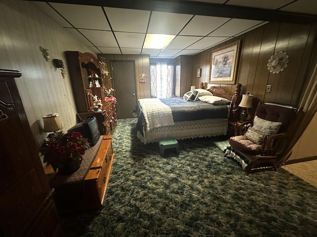 carpeted bedroom featuring wood walls and a drop ceiling