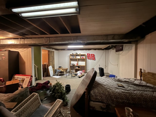 basement featuring stainless steel refrigerator and wooden walls