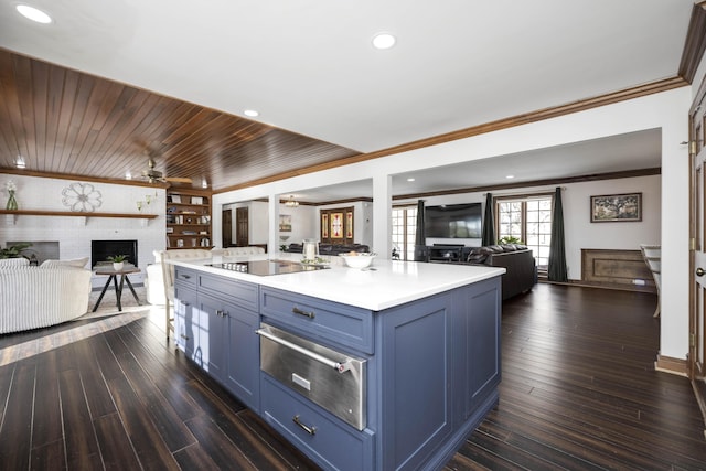 kitchen featuring dark hardwood / wood-style flooring, blue cabinetry, a fireplace, a center island with sink, and black electric cooktop