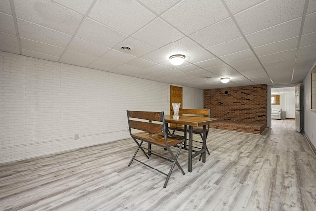 dining area with brick wall, light hardwood / wood-style flooring, and a drop ceiling