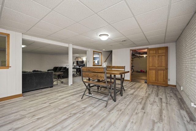 dining room featuring a paneled ceiling, brick wall, and light hardwood / wood-style floors