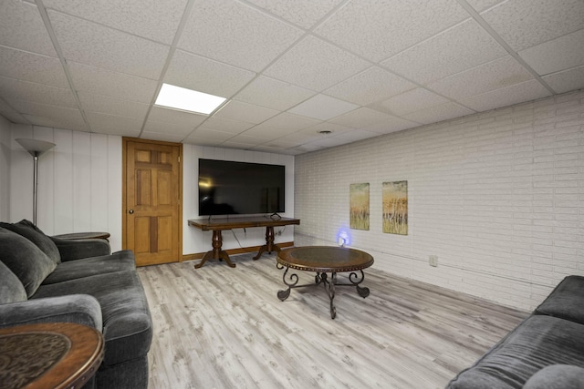 living room featuring light wood-type flooring, a paneled ceiling, and brick wall