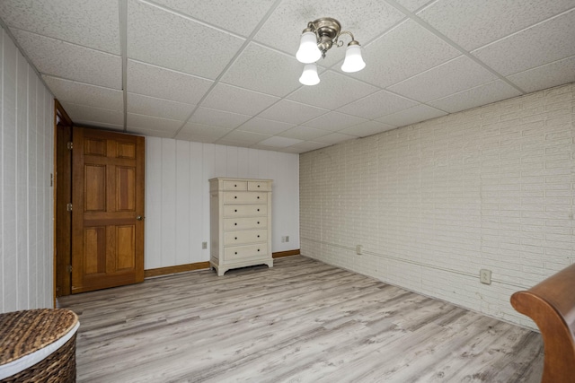 unfurnished bedroom with brick wall, a paneled ceiling, and light wood-type flooring