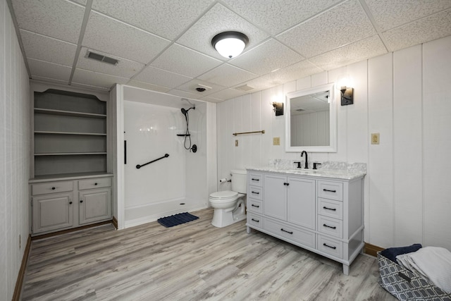 bathroom with a paneled ceiling, wood-type flooring, vanity, walk in shower, and toilet