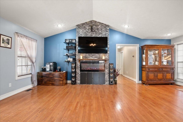 living room featuring a fireplace, vaulted ceiling, a textured ceiling, and light wood-type flooring