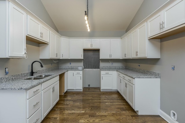 kitchen featuring vaulted ceiling, sink, white cabinetry, hanging light fixtures, and light stone countertops