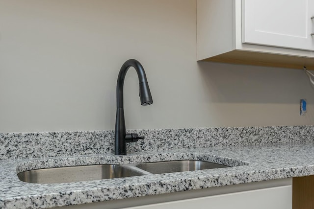 room details featuring sink, white cabinetry, and light stone countertops