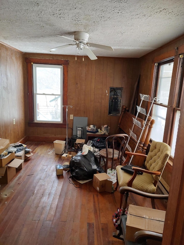 living area with ceiling fan, wood-type flooring, a textured ceiling, and wood walls