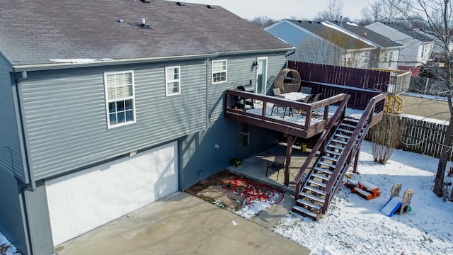 snow covered back of property featuring a garage and a deck