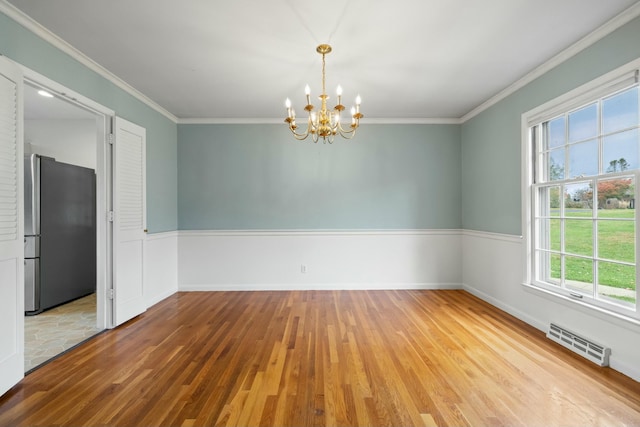 empty room featuring an inviting chandelier, crown molding, hardwood / wood-style floors, and a wealth of natural light