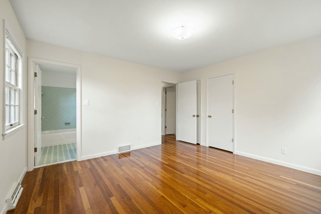 unfurnished bedroom with baseboard heating, ensuite bath, and hardwood / wood-style floors