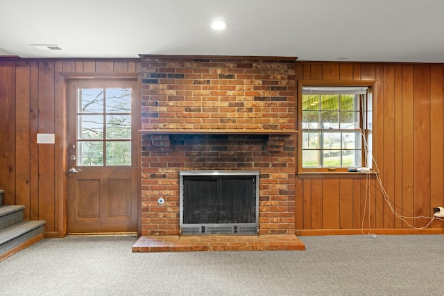 unfurnished living room featuring carpet floors, a fireplace, wooden walls, and a healthy amount of sunlight