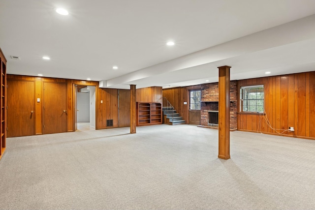 basement featuring a brick fireplace, light colored carpet, and wooden walls