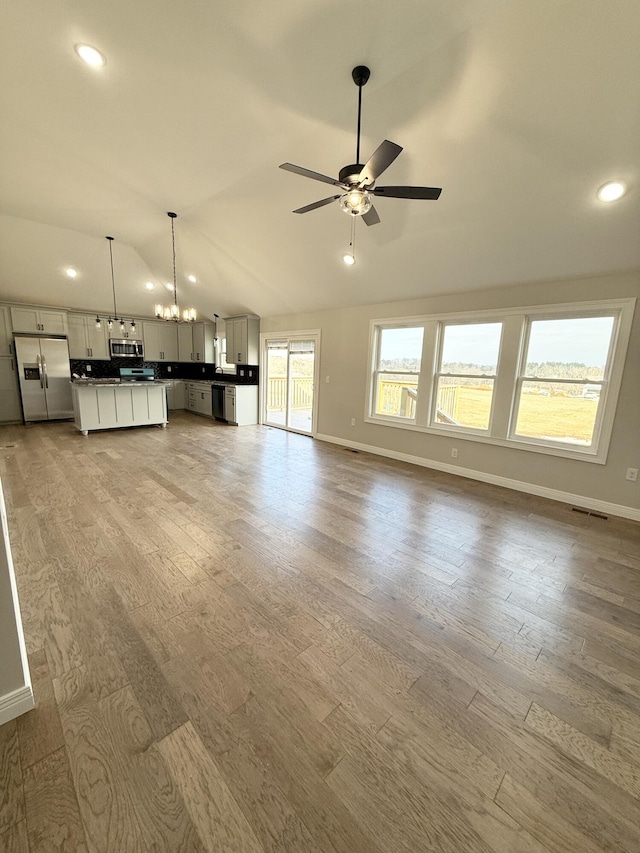 unfurnished living room featuring hardwood / wood-style flooring, lofted ceiling, and ceiling fan with notable chandelier