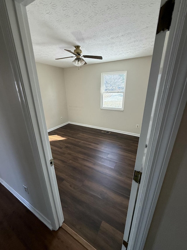 empty room featuring ceiling fan, dark wood-type flooring, and a textured ceiling