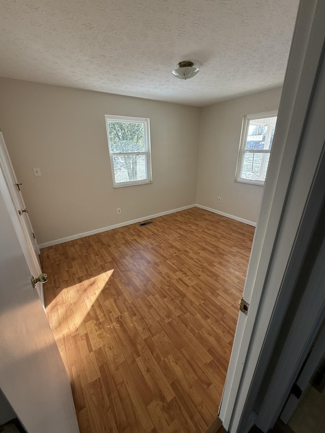 empty room with wood-type flooring, a textured ceiling, and a wealth of natural light