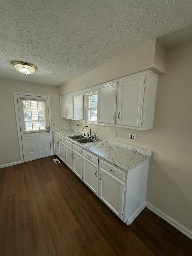 kitchen featuring sink, a textured ceiling, dark hardwood / wood-style flooring, light stone countertops, and white cabinets