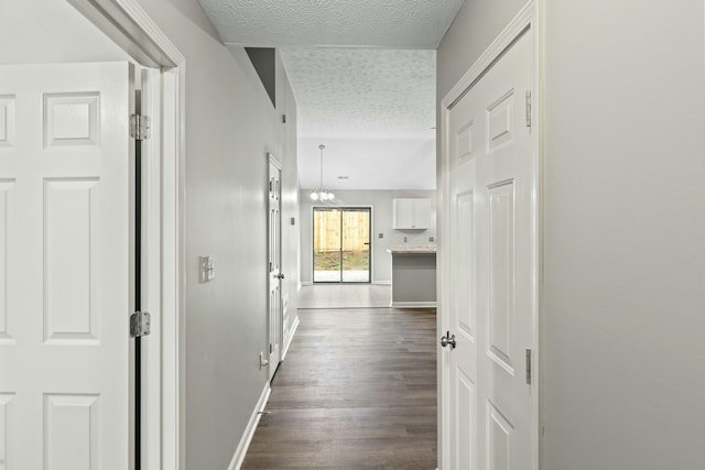 hall featuring an inviting chandelier, dark wood-type flooring, and a textured ceiling