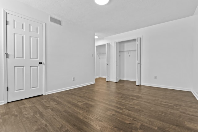 unfurnished bedroom with multiple closets, dark hardwood / wood-style floors, and a textured ceiling