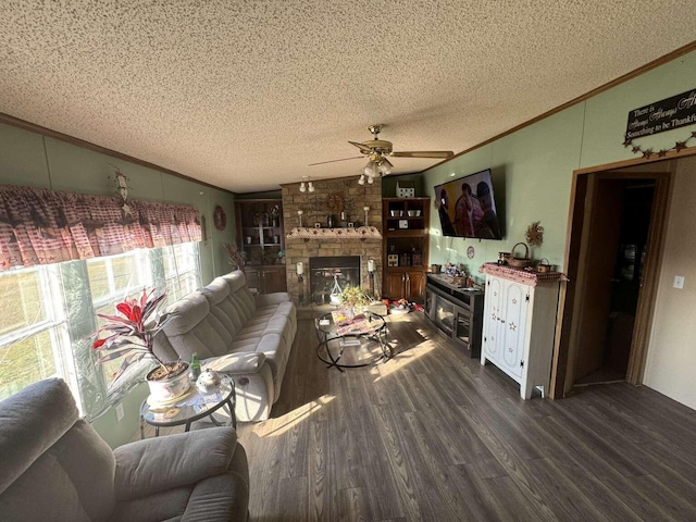 living room with a stone fireplace, ornamental molding, ceiling fan, dark wood-type flooring, and a textured ceiling