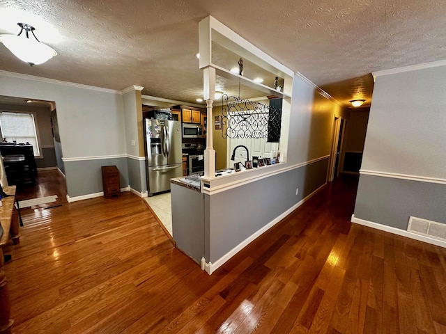 kitchen featuring hardwood / wood-style flooring, stainless steel appliances, crown molding, and a textured ceiling