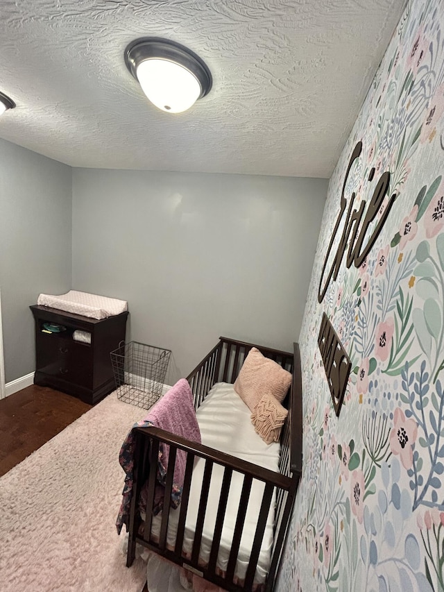 bedroom featuring a nursery area and a textured ceiling