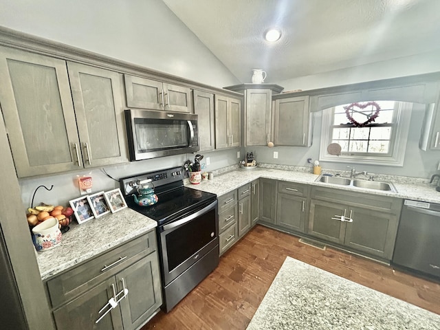 kitchen with sink, appliances with stainless steel finishes, dark hardwood / wood-style floors, light stone countertops, and vaulted ceiling