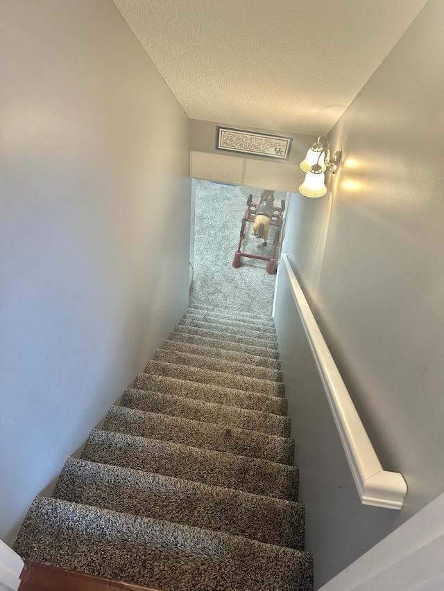 stairway with carpet and a textured ceiling