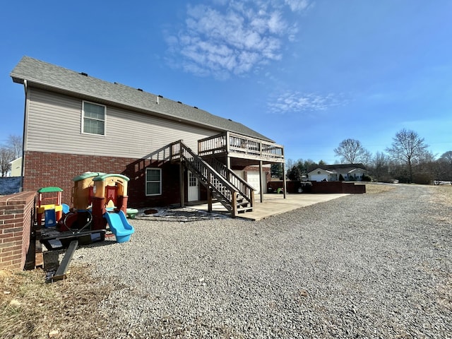 rear view of house with a wooden deck, a playground, and a patio