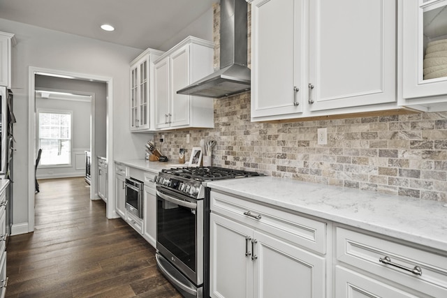 kitchen with appliances with stainless steel finishes, dark hardwood / wood-style floors, white cabinets, light stone counters, and wall chimney range hood