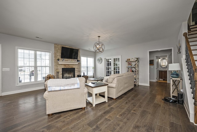 living room featuring an inviting chandelier, dark hardwood / wood-style floors, and a stone fireplace