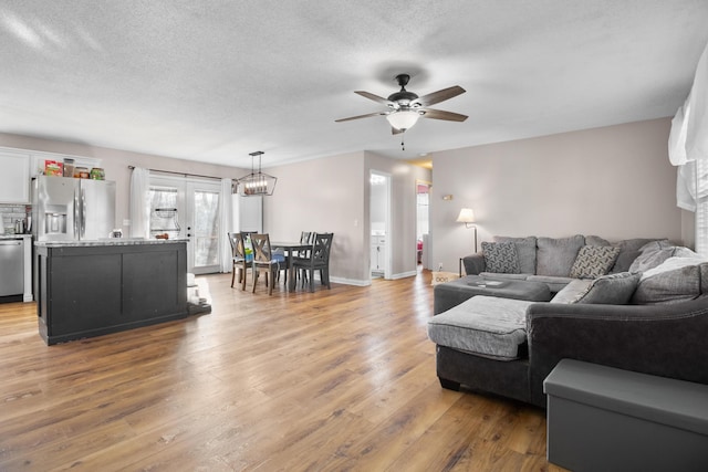 living room featuring ceiling fan with notable chandelier, a textured ceiling, and light hardwood / wood-style flooring